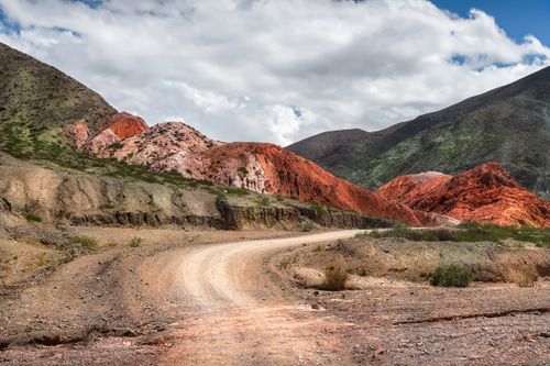 Free Unpaved road winding through colorful rock formations in a vibrant mountainous landscape under a blue sky. Stock Photo