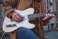 Person in Brown Leather Jacket Playing White Stratocaster Electric Guitar