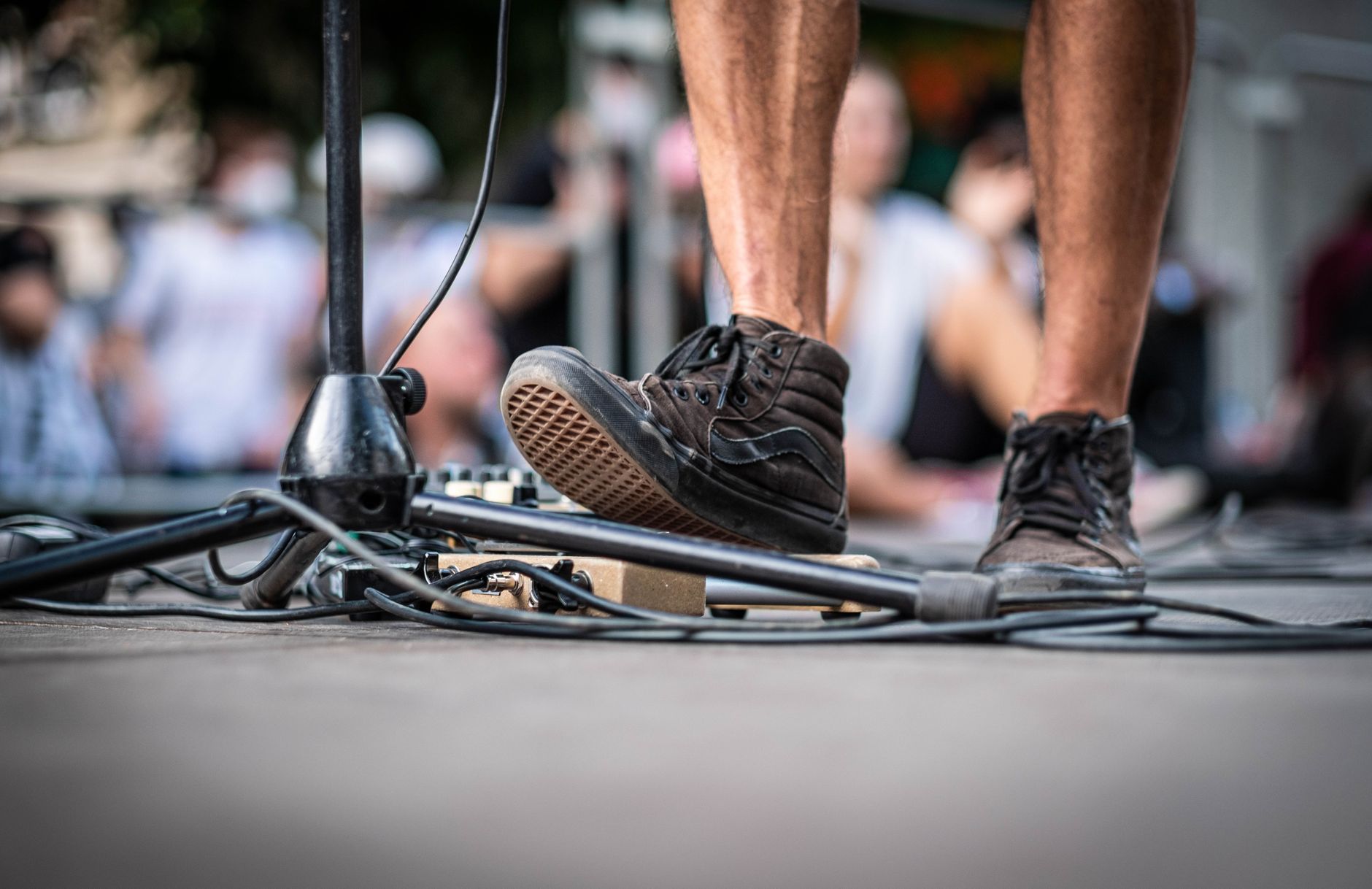 Close-up of a musician's black sneakers on stage with a microphone stand and guitar gear.