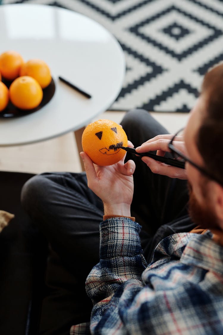 Man Holding An Orange Fruit And Drawing On It