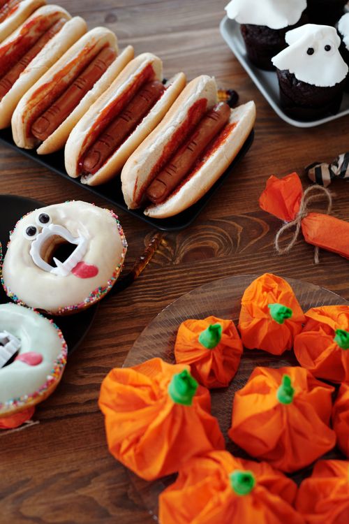 Free Creative Halloween-themed snacks including hotdogs, ghost cupcakes, and pumpkin treats. Stock Photo