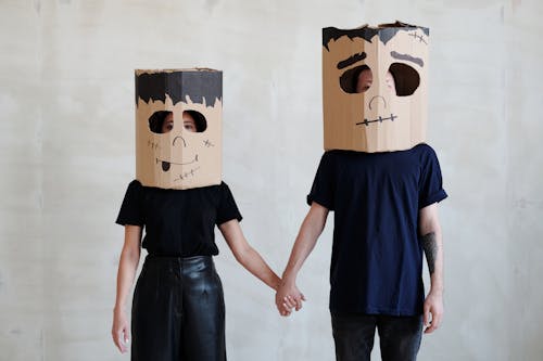 A Couple Wearing Diy Cardboard Box Mask While Holding Each Other's Hands