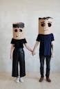 A Couple Wearing Diy Cardboard Box Mask While Holding Each Other's Hands