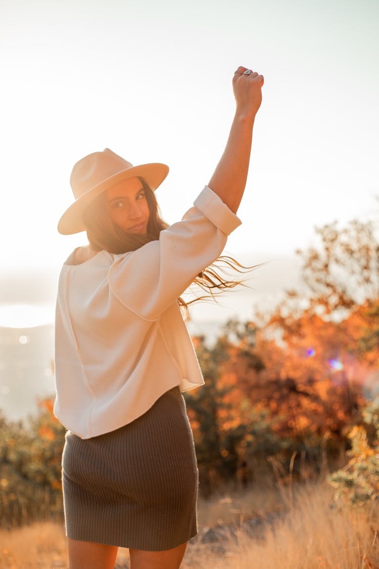 Young Woman Standing In A Field And Raising Arm At Fall