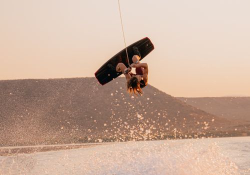 Free Wakeboarder performing a backflip during golden hour on a scenic lake. Stock Photo