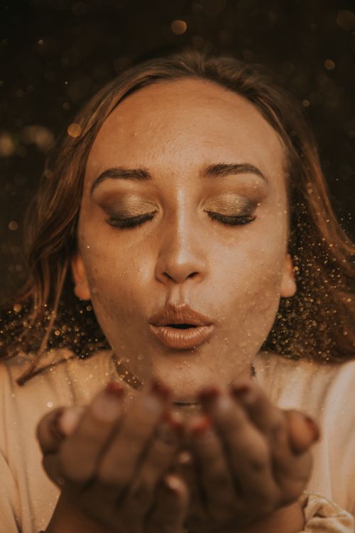 Free A fashionable woman with closed eyes blowing glitter, creating a mesmerizing visual effect. Stock Photo