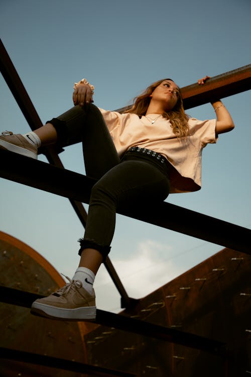 A Woman in White Shirt and Black Pants Sitting on Black Metal Bar