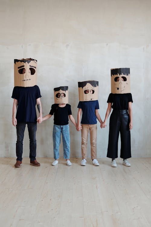 Una Familia Con Una Máscara De Caja De Cartón Hecha Por Uno Mismo Mientras Se Toman De La Mano