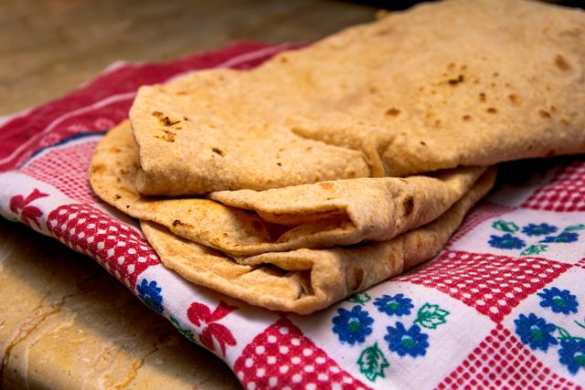 Freshly made chapati placed on a vibrant patterned cloth, highlighting its texture and homemade appeal.
