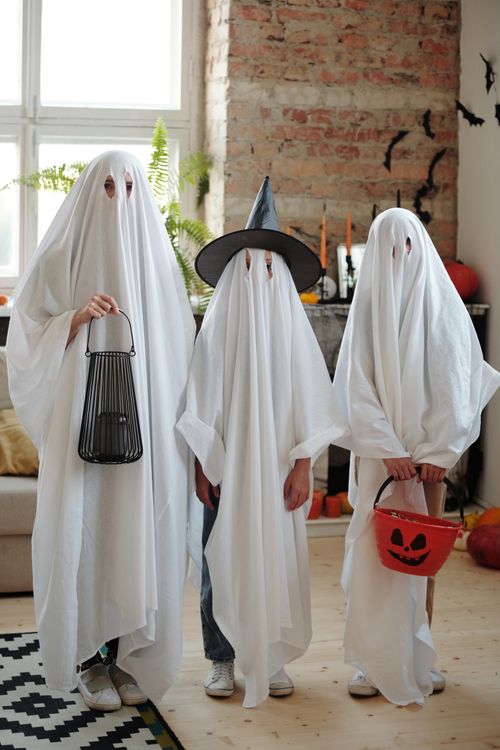 Free Three children in ghost costumes with Halloween buckets inside a home. Stock Photo