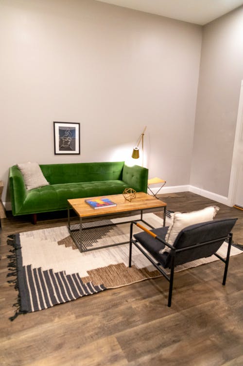 Living room interior design with small framed photo above cozy green sofa and wooden table on soft carpet