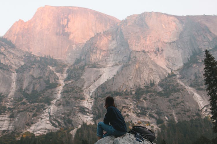 Anonymous Hiker Recreating On Rocky Cliff And Enjoying Mountain View At Sundown