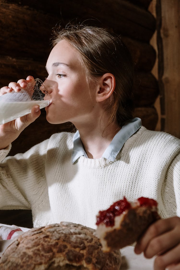 Girl In White Sweater Drinking Milk And Eating Bread With Jam