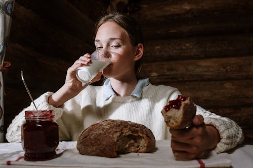 Girl Sitting at the Table and Eating Bread with Jam and Drinking Milk 