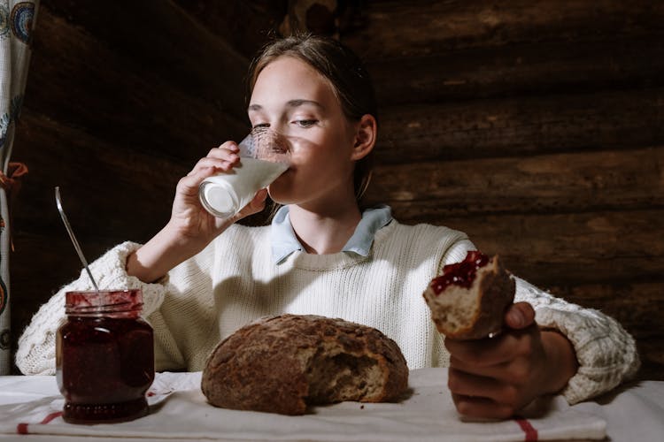 Girl Sitting At The Table And Eating Bread With Jam And Drinking Milk 