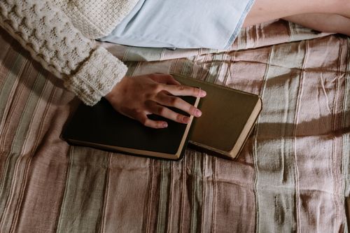 Free A cozy scene of a person in a wool sweater holding a hardcover book on a bed. Stock Photo