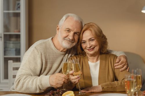 Free Smiling senior couple toasting with champagne glasses indoors, symbolizing love and celebration. Stock Photo