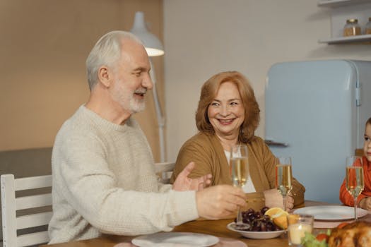 Elderly couple enjoying a joyful family dinner with champagne and fruit.