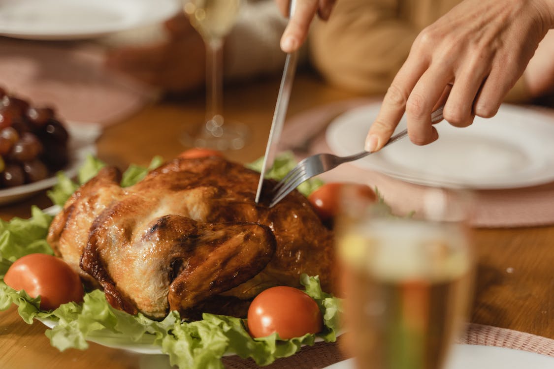 Free Close-up of hands slicing delicious roasted chicken with vegetables on a festive table setting. Stock Photo