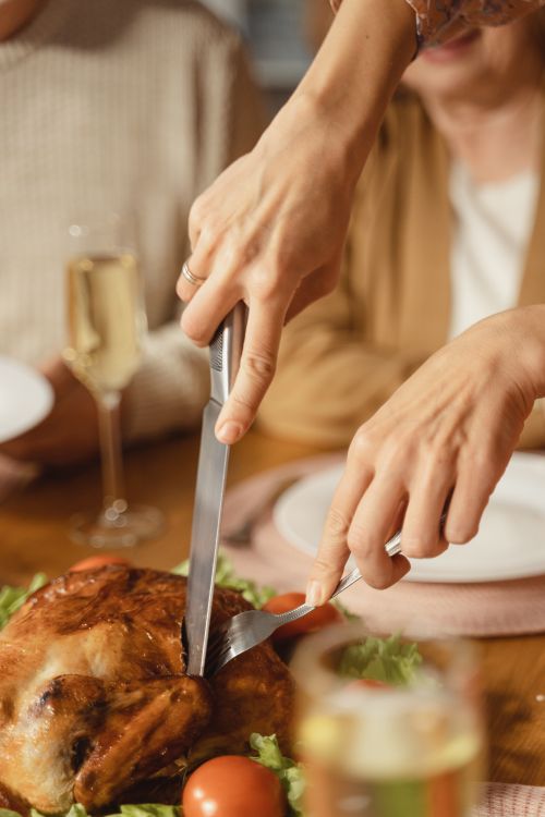 Free Close-up of hands slicing a holiday roast turkey at a festive family dinner table. Stock Photo