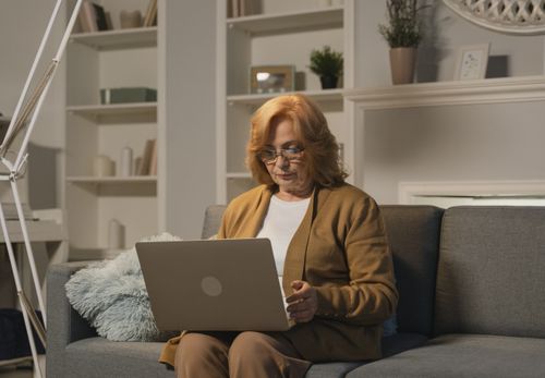 Free Senior woman with eyeglasses working on a laptop in a cozy living room setting. Stock Photo