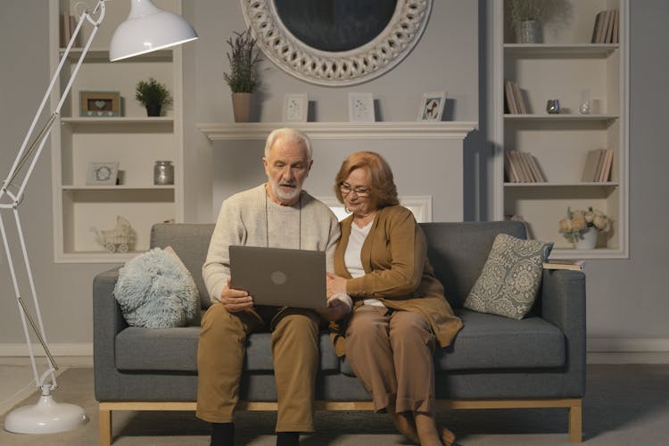 An Elderly Couple Sitting On A Couch While Looking At The Screen Of A Laptop