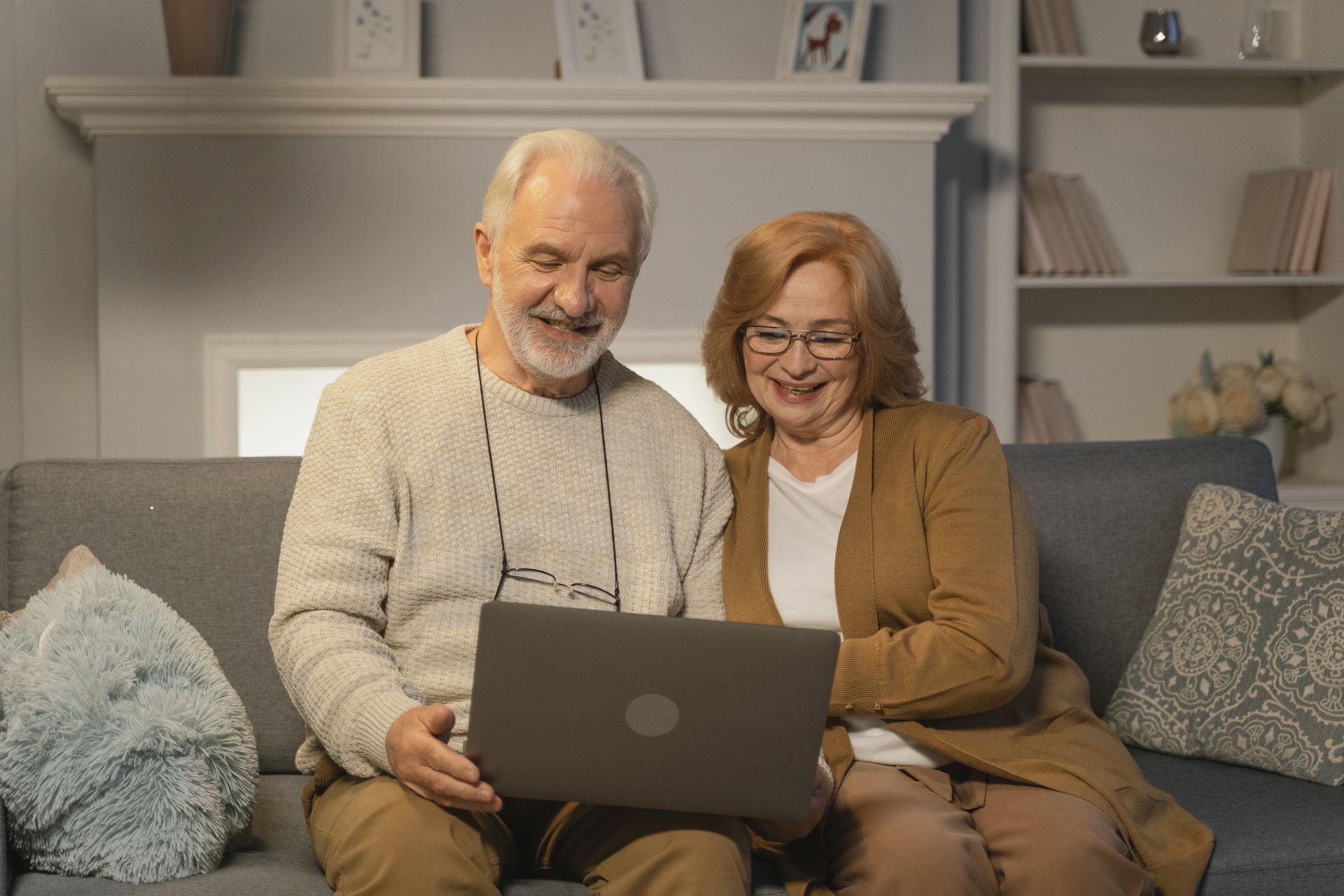 Elderly couple enjoying a moment together on a cozy couch, using a laptop, and smiling.