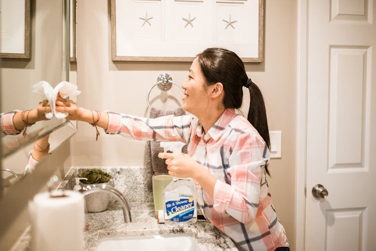 Woman Smiling While Cleaning The Mirror