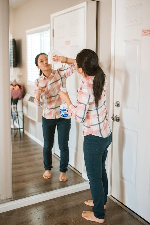 Woman Cleaning the Mirror While Holding Spray Bottle