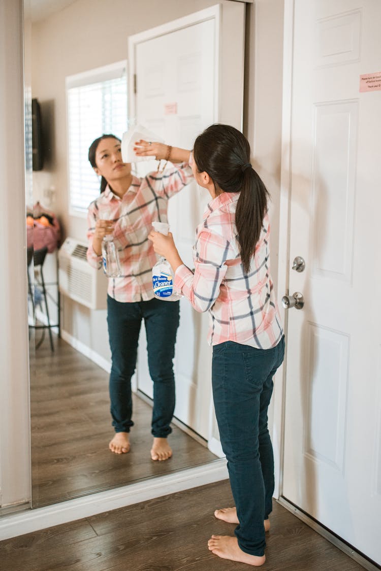 Woman Cleaning The Mirror While Holding Spray Bottle