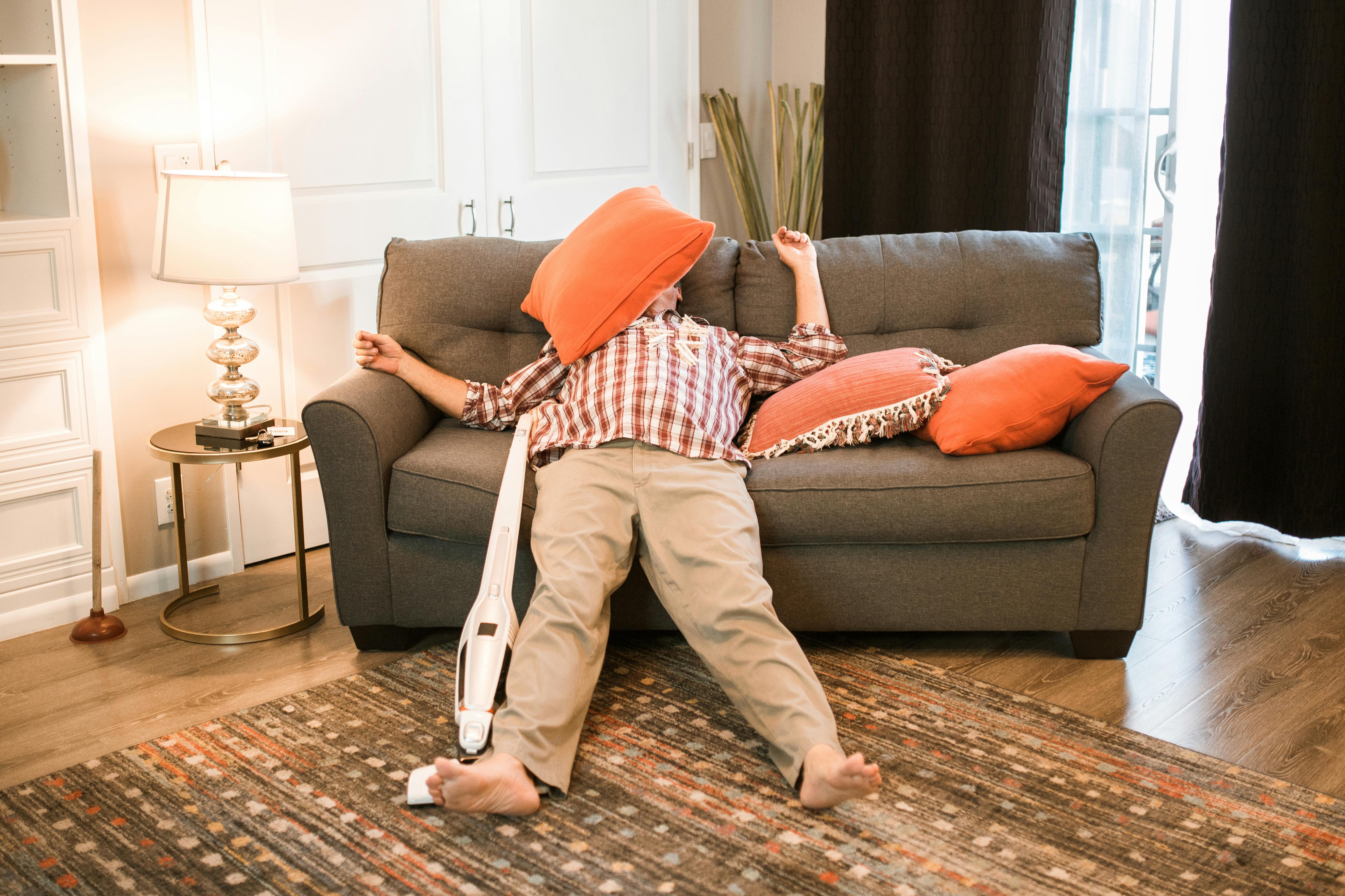 man lying on sofa beside vacuum