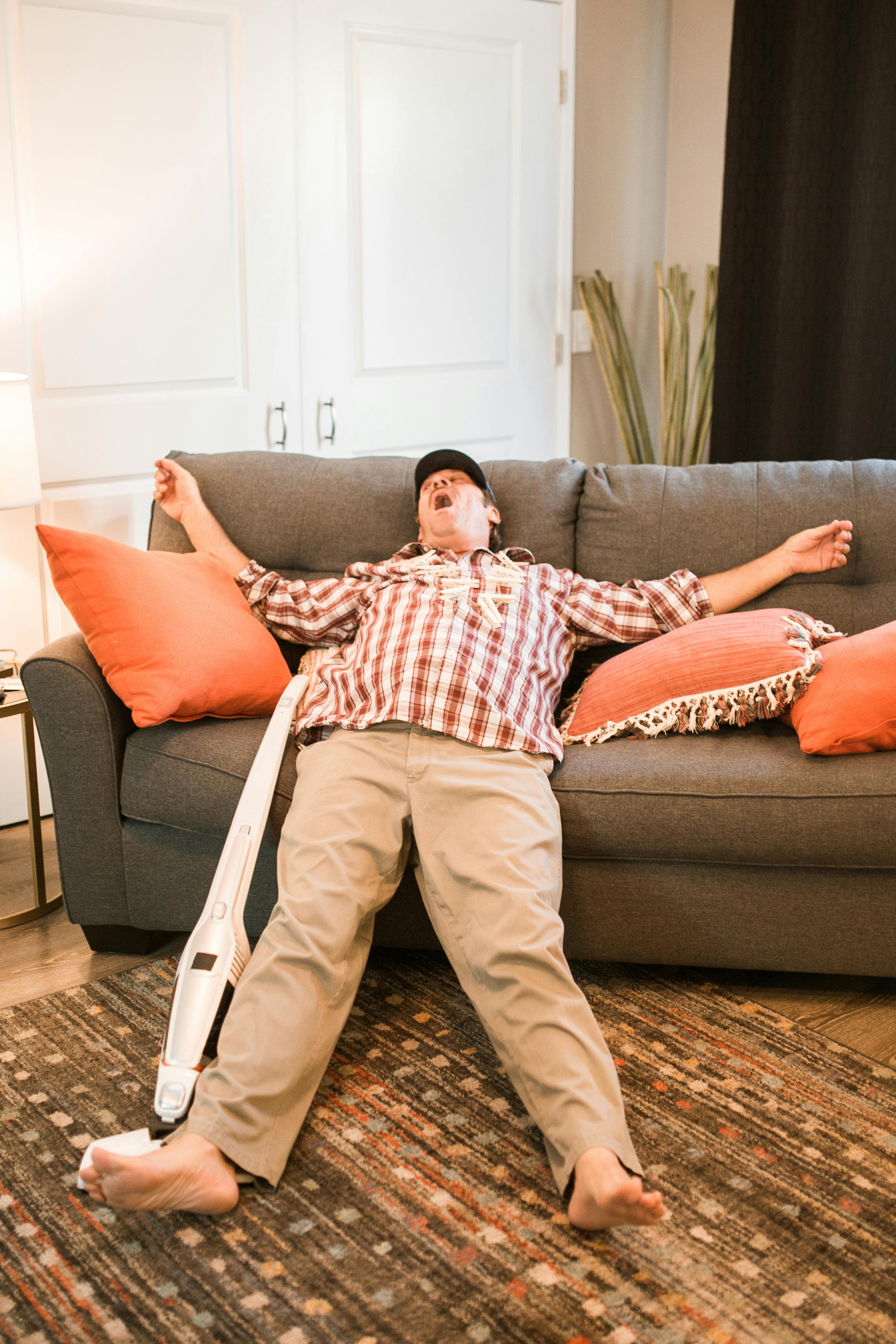 man in red white and black plaid dress shirt and brown pants sitting on brown couch
