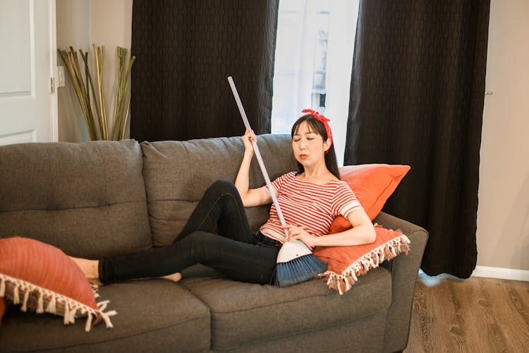 Woman Sitting On Sofa Holding A Broom