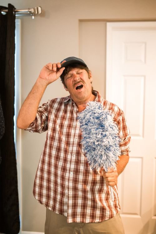 Free A man humorously sings into a duster, embodying joyful house cleaning. Stock Photo