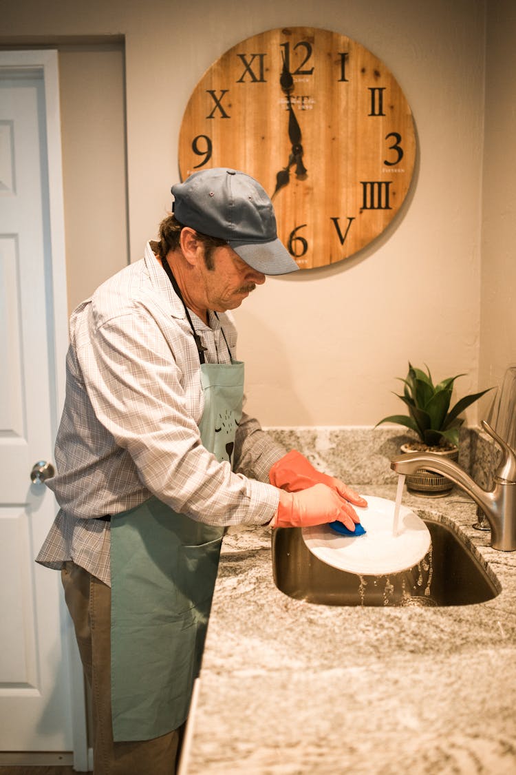 A Man Wearing A Cap Washing A Plate