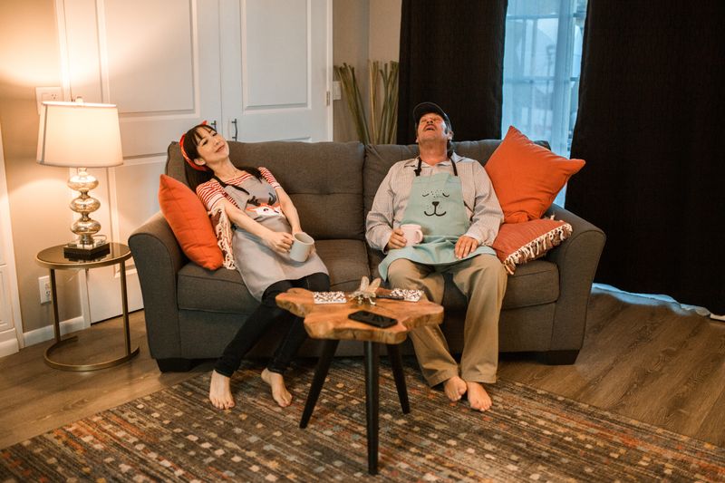 A couple in aprons relaxing on a sofa with coffee, embodying a cozy home atmosphere.