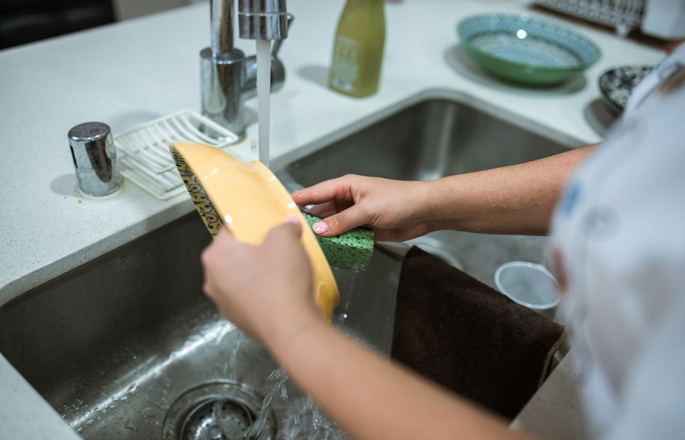 Hands washing dishes at a bright kitchen sink.