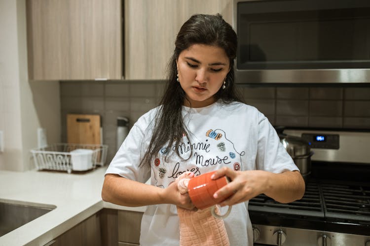 A Woman Wearing A White Shirt Cleaning A Red Mug