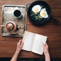 Hands holding an open book beside a teapot, photo by Ekrulila on Pexels