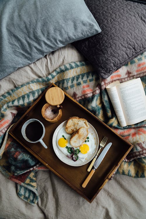 Tray with breakfast on bed near book