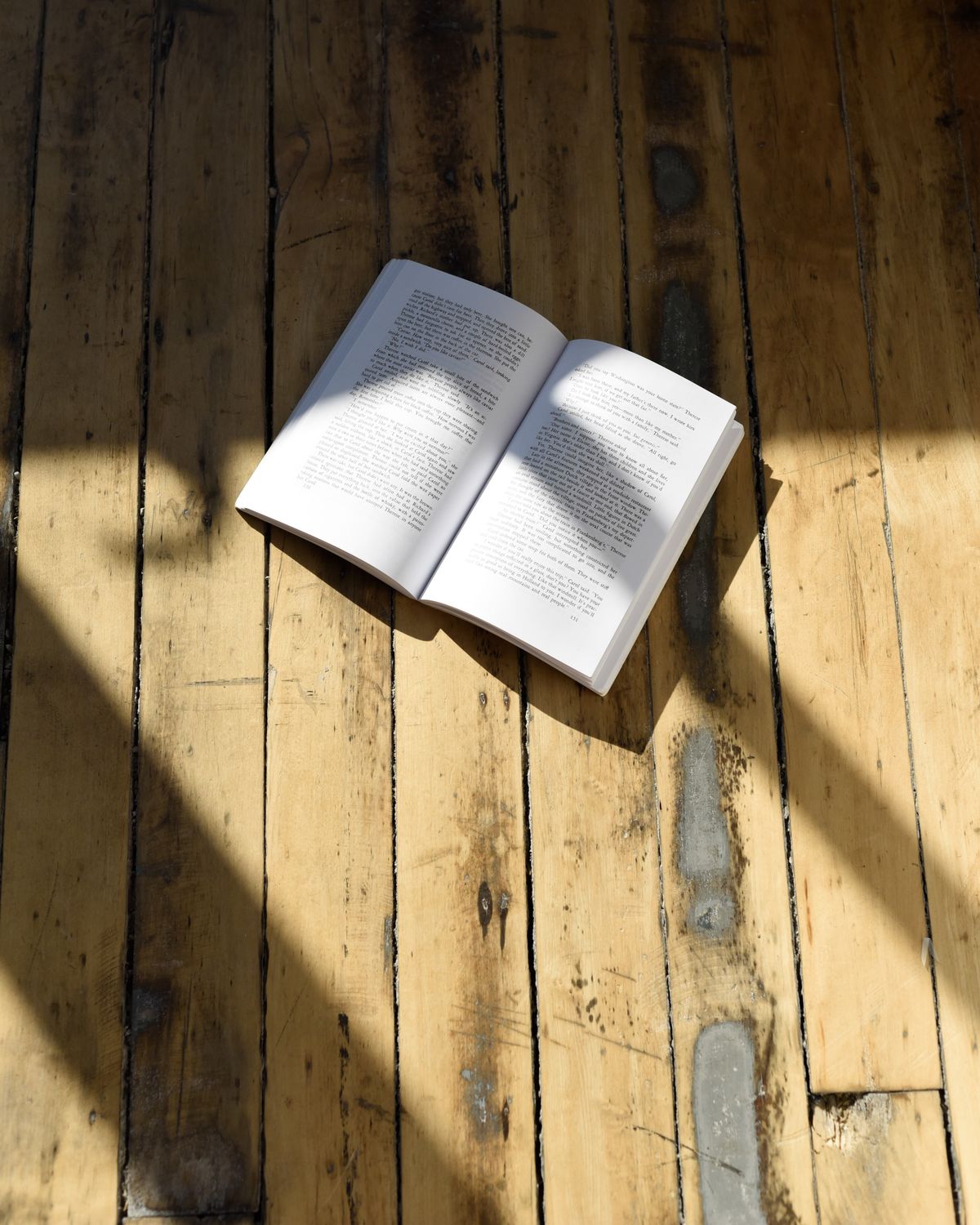 An open volume on a sunlit plank floor — photo by Daniela Constantini on Pexels