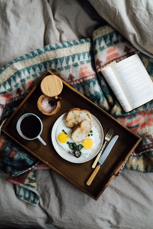 Free From above of fresh breakfast from fried eggs with bread near coffee and opened book on blanket Stock Photo