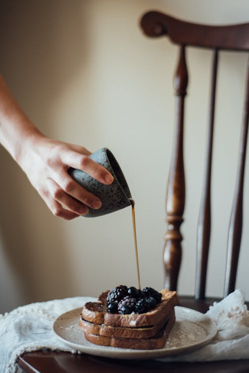 Free Crop unrecognizable person holding mug and pouring syrup on toasts with fresh blackberry Stock Photo