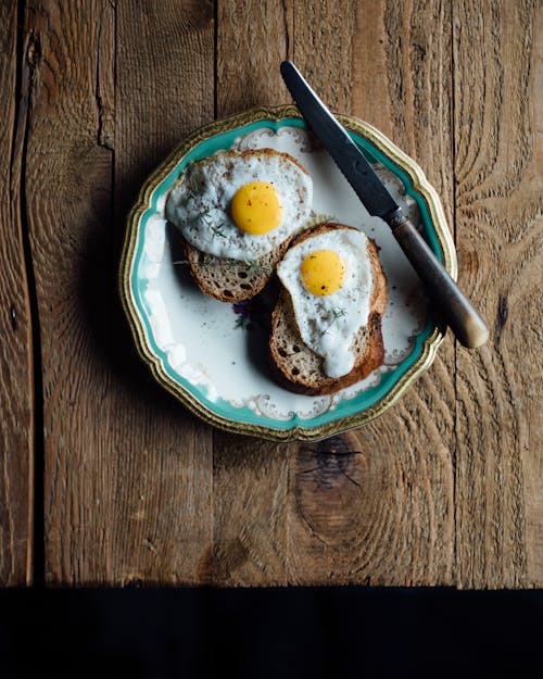 Free From above of appetizing fried eggs on toasts in plate near knife on wooden table Stock Photo