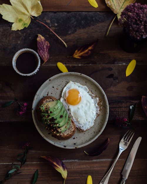 Free Top view of avocado toast with fried eggs and mug of fresh coffee with bright autumn leaves on wooden table Stock Photo