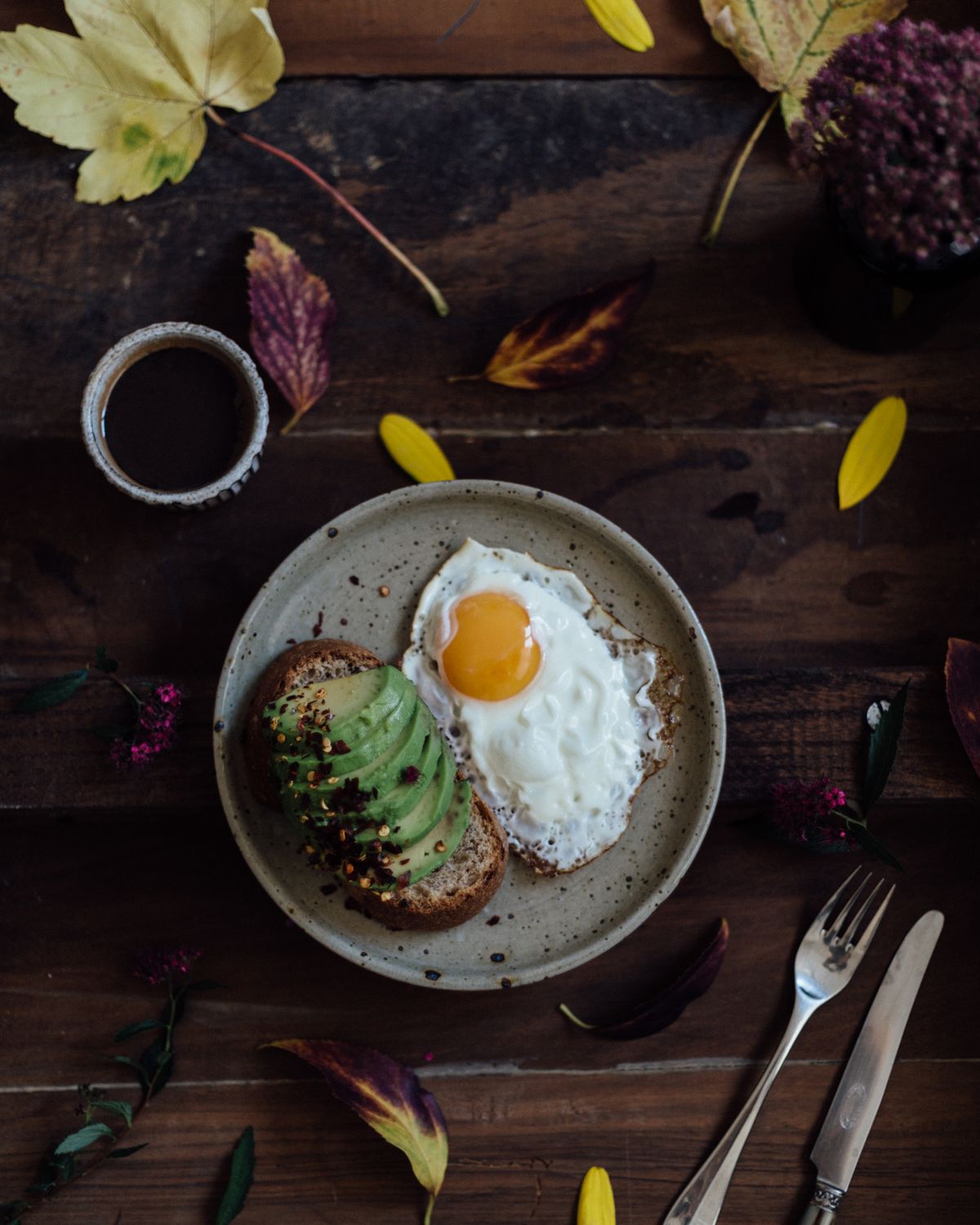 Person eating a bowl of yogurt and fruit at a breakfast table with coffee