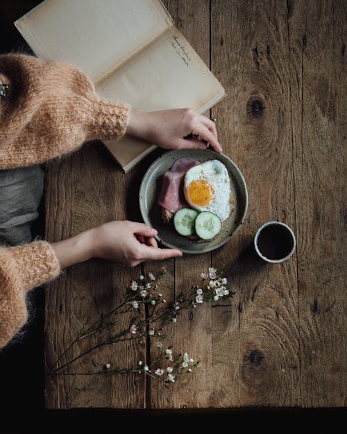 Free Crop woman at table with book and breakfast Stock Photo