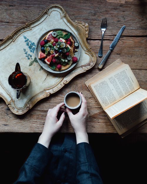 Free From above of crop faceless female holding cup of hot coffee on table with book and salad with fresh fruits Stock Photo