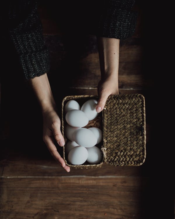 Crop person holding chicken eggs in basket