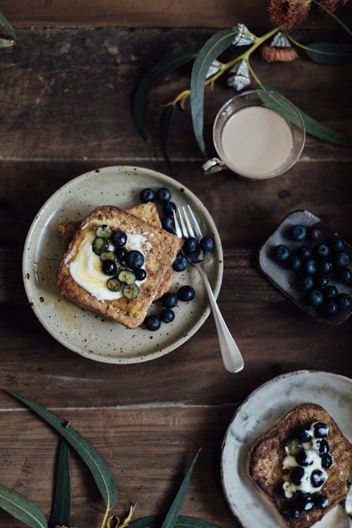 Free From above of delicious toasts with berries on plate and cup of coffee near fresh green plants on wooden table Stock Photo